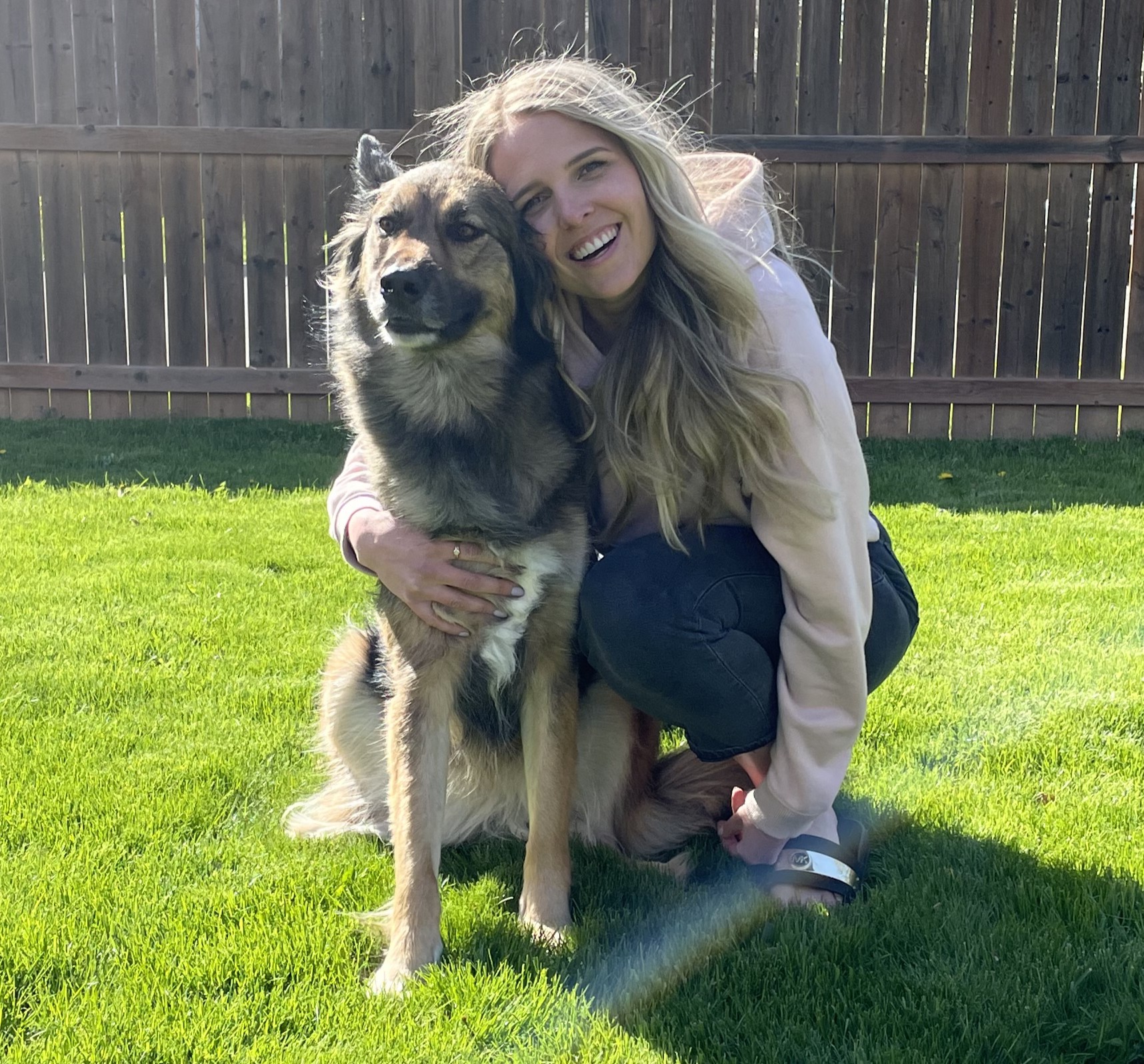 A women with blond hair crouched beside a large dog, outdoors